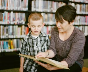 Teacher or parent with young boy looking at a book in a library